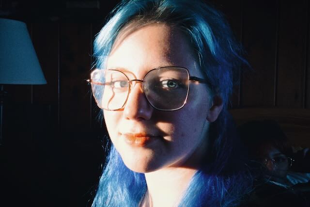 Abigail with blue hair, looking into the camera, light on half of her face.